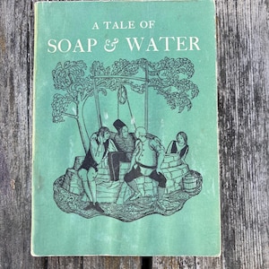 Op de afbeelding: Vintage boekomslag met de titel "A Tale of Soap & Water" in wit op een zeegroene achtergrond. De omslag toont een zwart-wit illustratie van mensen rond een put.