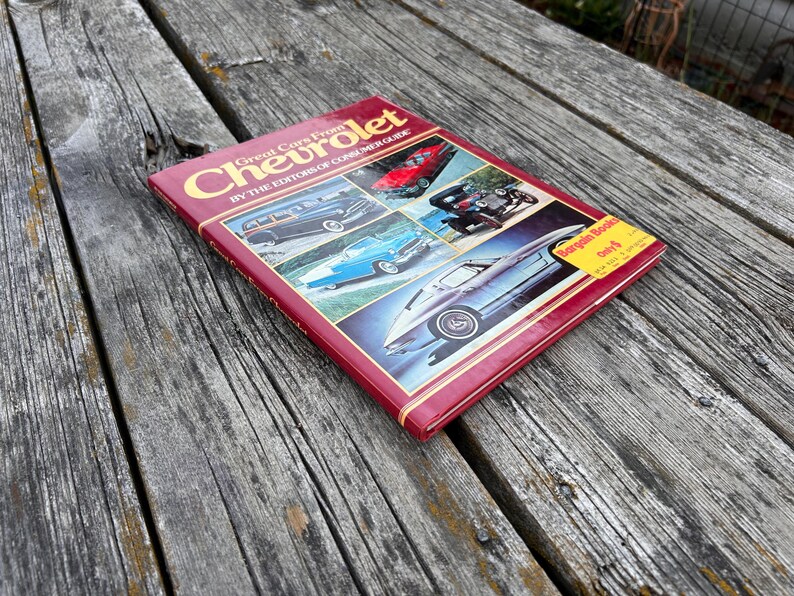 Op de afbeelding: Een rood hardcover boek getiteld Great Cars From Chevrolet by the Editors of Consumer Guide. De kaft bevat vier kleurenfoto's van vintage Chevrolet-auto's en een gele ronde sticker met de tekst Bargain Books Only $.