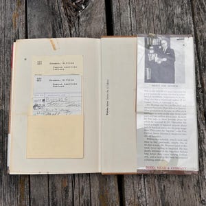 Puede incluir: Un libro de tapa dura abierto que presenta una tarjeta de pr&eacute;stamo de biblioteca en un bolsillo en la p&aacute;gina izquierda y una biograf&iacute;a del autor con una fotograf&iacute;a en blanco y negro en la solapa derecha. El texto incluye William Heuman, Famous American Indians.