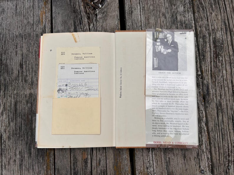 Puede incluir: Un libro de tapa dura abierto que presenta una tarjeta de pr&eacute;stamo de biblioteca en un bolsillo en la p&aacute;gina izquierda y una biograf&iacute;a del autor con una fotograf&iacute;a en blanco y negro en la solapa derecha. El texto incluye William Heuman, Famous American Indians.