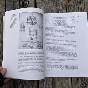 K&ouml;nnte beinhalten: Ein aufgeschlagenes Buch mit wei&szlig;en Seiten, schwarzem Text und einer schwarz-wei&szlig;en architektonischen Skizze einer Kathedrale. Die linke Seite zeigt ein Diagramm eines Geb&auml;udes, w&auml;hrend die rechte Seite Spalten mit Dialogtext enth&auml;lt.