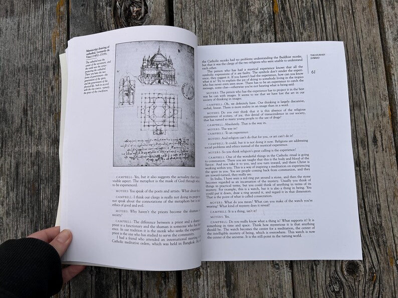 K&ouml;nnte beinhalten: Ein aufgeschlagenes Buch mit wei&szlig;en Seiten, schwarzem Text und einer schwarz-wei&szlig;en architektonischen Skizze einer Kathedrale. Die linke Seite zeigt ein Diagramm eines Geb&auml;udes, w&auml;hrend die rechte Seite Spalten mit Dialogtext enth&auml;lt.