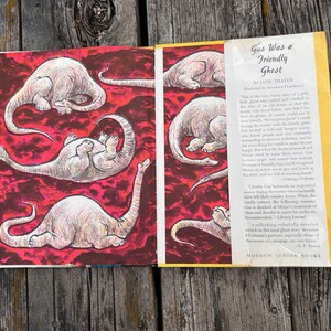 Pode incluir: Um livro de capa dura intitulado Gus Was a Friendly Ghost de Jane Thayer, ilustrado por Seymour Fleishman. A sobrecapa aberta exibe um fundo vermelho vibrante com v&aacute;rias ilustra&ccedil;&otilde;es de uma criatura p&aacute;lida de pesco&ccedil;o longo.