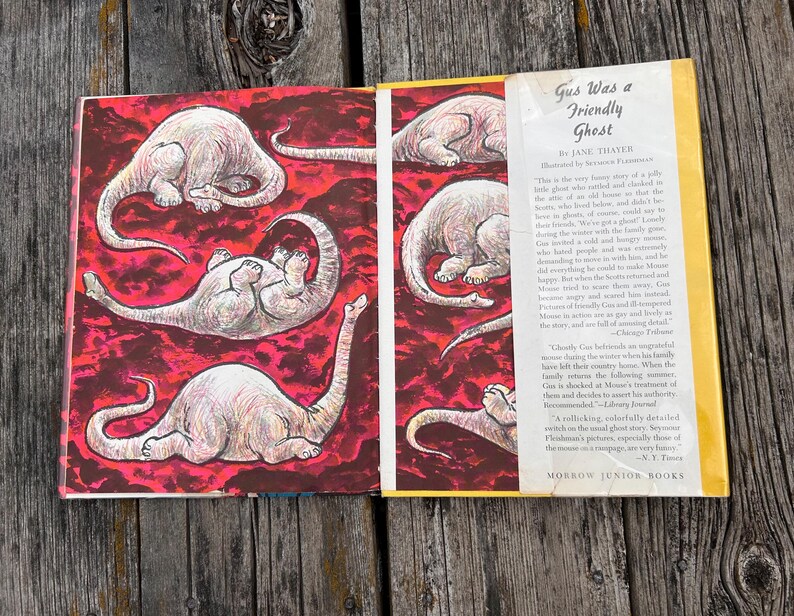 Pode incluir: Um livro de capa dura intitulado Gus Was a Friendly Ghost de Jane Thayer, ilustrado por Seymour Fleishman. A sobrecapa aberta exibe um fundo vermelho vibrante com v&aacute;rias ilustra&ccedil;&otilde;es de uma criatura p&aacute;lida de pesco&ccedil;o longo.