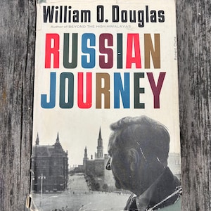 May include: A book titled Russian Journey by William O. Douglas with a white cover featuring bold, multi-coloured lettering. The cover displays a black and white photograph of a man in profile overlooking a city square with tall, pointed towers.
