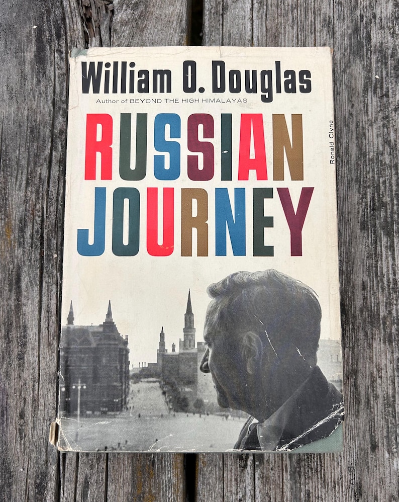 May include: A book titled Russian Journey by William O. Douglas with a white cover featuring bold, multi-coloured lettering. The cover displays a black and white photograph of a man in profile overlooking a city square with tall, pointed towers.