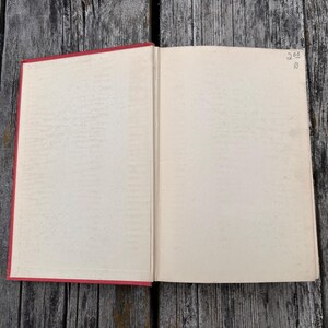 May include: An open book with a red spine and cover edges, featuring blank, off-white pages. The top right corner of the right page contains handwritten text that reads 200 over 10. The book is displayed flat, showing the interior binding and paper.