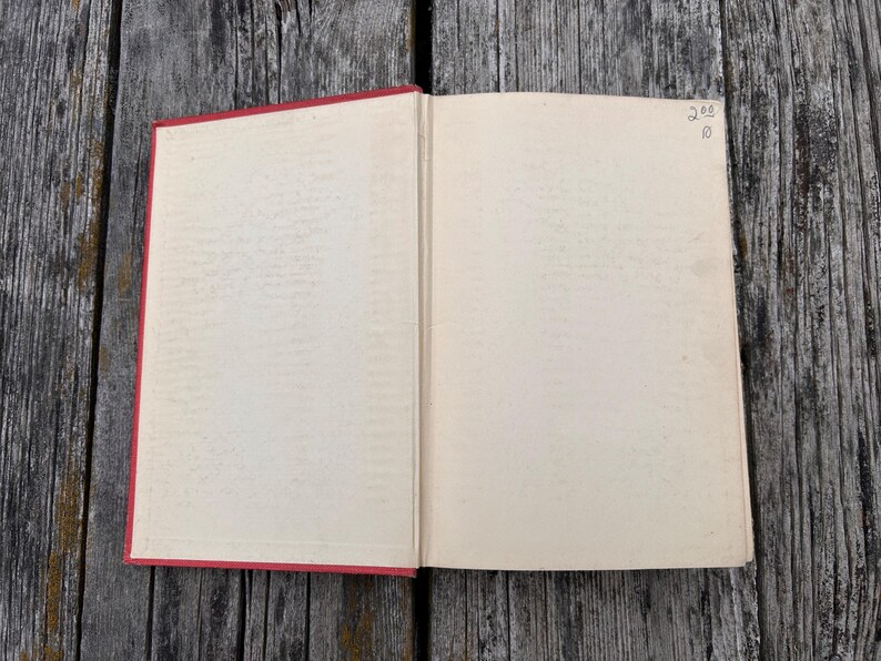 May include: An open book with a red spine and cover edges, featuring blank, off-white pages. The top right corner of the right page contains handwritten text that reads 200 over 10. The book is displayed flat, showing the interior binding and paper.