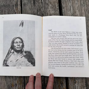Może przedstawiać: Otwarta książka z dwiema stronami, przedstawiająca czarno-biały portret wodza Galla po lewej stronie oraz tekst biograficzny zatytułowany Gall po prawej stronie. Tekst opisuje historię przyw&oacute;dcy Hunkpapa Teton Sioux i jego rolę w bitwie nad Little Bighorn.