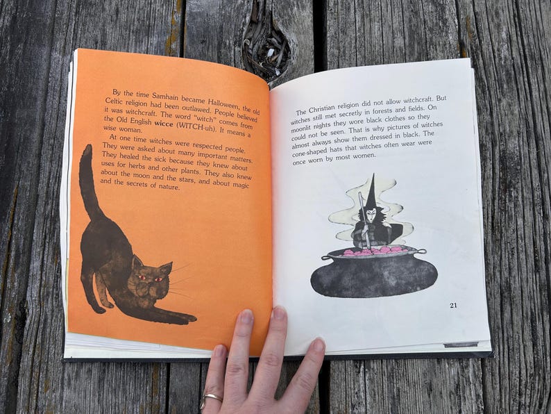 May include: An open book with two pages of text. The left page has an orange background and an illustration of a black cat with red eyes. The right page is white with black text and an illustration of a witch stirring a black cauldron.