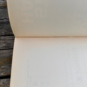 Peut inclure: Livre ouvert avec des pages blanc cass&eacute;, montrant le bord des pages et la reliure. Les pages sont l&eacute;g&egrave;rement courb&eacute;es. Le livre est pos&eacute; sur une surface en bois gris&eacute; et vieilli.