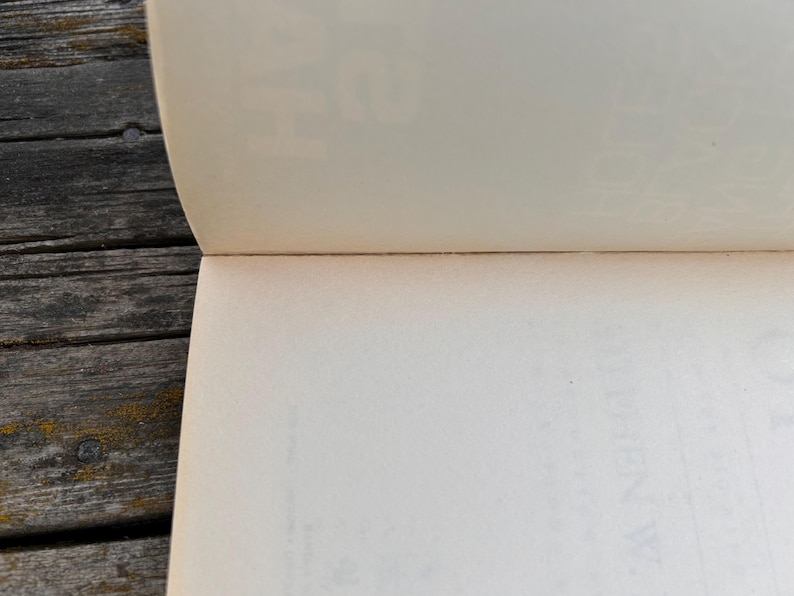Peut inclure: Livre ouvert avec des pages blanc cass&eacute;, montrant le bord des pages et la reliure. Les pages sont l&eacute;g&egrave;rement courb&eacute;es. Le livre est pos&eacute; sur une surface en bois gris&eacute; et vieilli.
