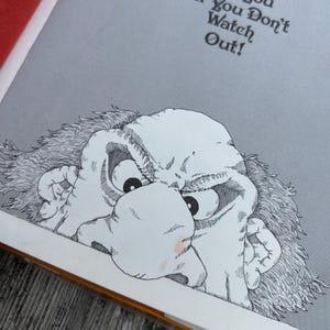 May include: A book page illustration featuring a black and white line drawing of a grumpy, wide-eyed character with messy hair peering from the bottom. Above the character, the text reads: The Gobble-uns'll Git You Ef You Don't Watch Out!