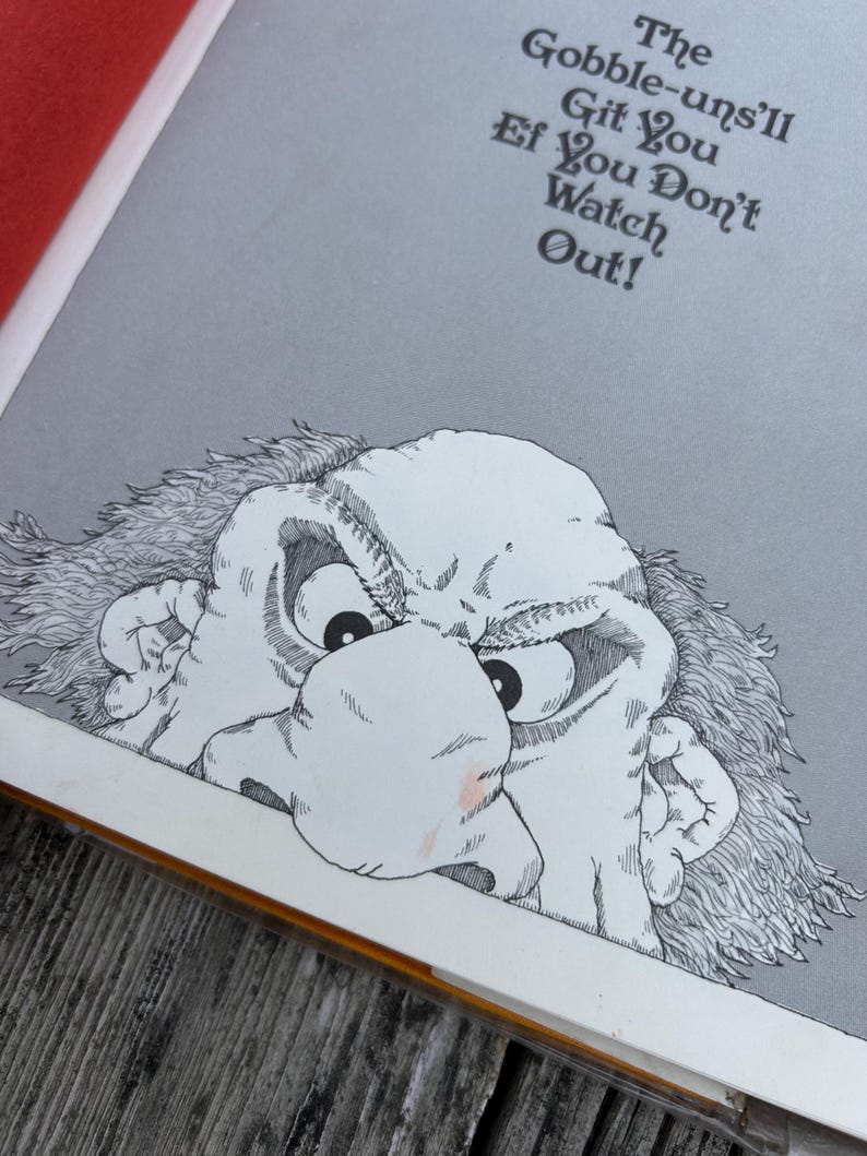 May include: A book page illustration featuring a black and white line drawing of a grumpy, wide-eyed character with messy hair peering from the bottom. Above the character, the text reads: The Gobble-uns'll Git You Ef You Don't Watch Out!