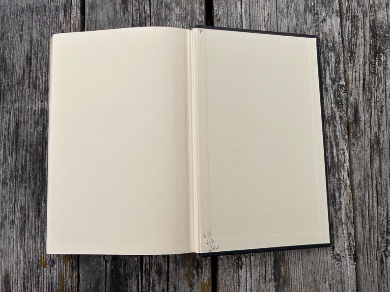 Pu&ograve; includere: Un libro aperto con pagine bianche color crema. Il dorso &egrave; visibile al centro e c'&egrave; una piccola scritta a mano nell'angolo in basso a destra della pagina di destra. Il libro ha una copertina scura ed &egrave; disposto in posizione piana.
