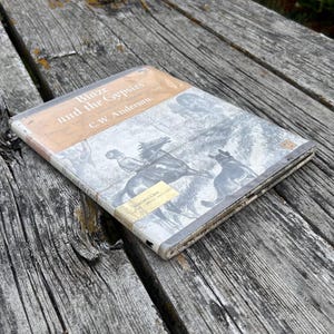 May include: A hardcover book titled Blaze and the Gypsies by C.W. Anderson. The cover features a black and white illustration of a person riding a horse with a dog nearby. The top section is tan, and a small yellow library sticker is on the bottom.
