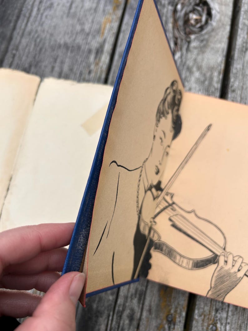 May include: A vintage book with a blue spine and a cream-coloured page featuring a black ink illustration of a person playing a violin. The drawing depicts the individual from the chest up, holding the instrument with a bow, rendered in fine lines.