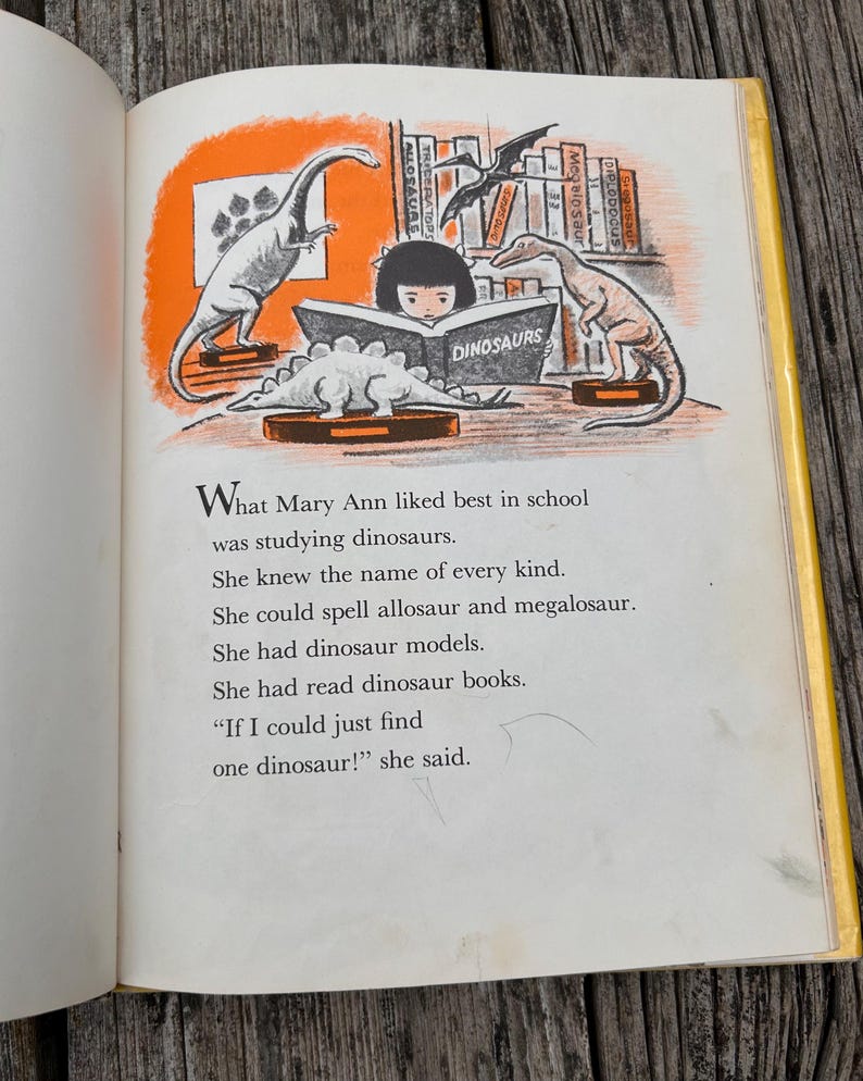 Pode incluir: Uma p&aacute;gina de um livro infantil com uma ilustra&ccedil;&atilde;o de uma crian&ccedil;a lendo um livro intitulado DINOSAURS, cercada por modelos de dinossauros em prateleiras e mesas. O texto diz: What Mary Ann liked best in school was studying dinosaurs.