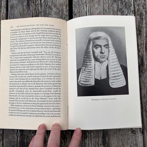 Pu&ograve; includere: Un libro aperto con pagine color crema, testo nero e un ritratto in bianco e nero di una persona che indossa una parrucca e una toga legale tradizionale. La didascalia sotto il ritratto recita: "Hastings as Attorney-General".