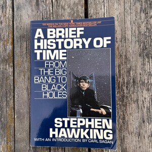 Peut inclure: Un livre de Stephen Hawking intitul&eacute; "Une br&egrave;ve histoire du temps". La couverture est bleu fonc&eacute; avec du texte blanc et jaune. On y voit une photo de Stephen Hawking et le texte "Du Big Bang aux trous noirs".
