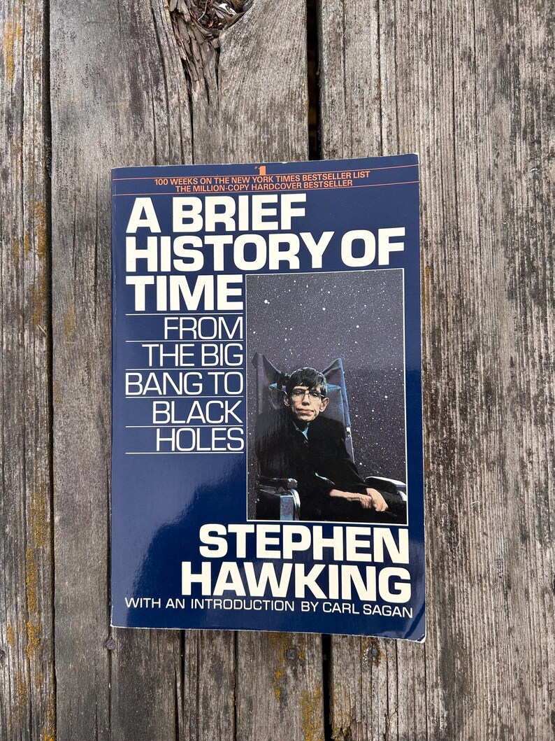 Peut inclure: Un livre de Stephen Hawking intitul&eacute; "Une br&egrave;ve histoire du temps". La couverture est bleu fonc&eacute; avec du texte blanc et jaune. On y voit une photo de Stephen Hawking et le texte "Du Big Bang aux trous noirs".