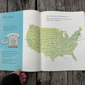 May include: An open book page featuring a light blue section with a white rotary telephone illustration and the text 6 ON THE PHONE. The right page displays a green map of the United States with area codes printed on each state and text asking about telephone area codes.
