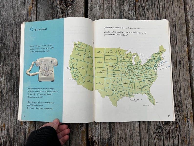 May include: An open book page featuring a light blue section with a white rotary telephone illustration and the text 6 ON THE PHONE. The right page displays a green map of the United States with area codes printed on each state and text asking about telephone area codes.