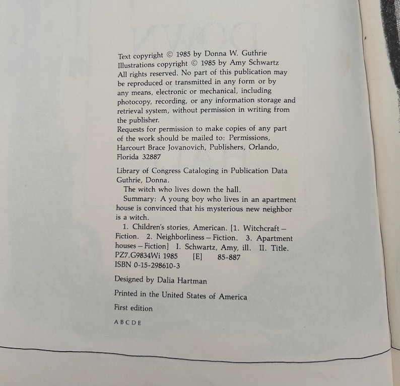 Puede incluir: Una p&aacute;gina de libro blanca con texto impreso en negro que incluye informaci&oacute;n de derechos de autor para el libro The Witch Who Lives Down the Hall de Donna W. Guthrie, ilustrado por Amy Schwartz, publicado en 1985, con datos de la biblioteca.