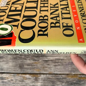 May include: A hardcover book titled Any Four Women Could Rob the Bank of Italy by Ann Cornelisen. The cover is yellow with black text and a red stripe. A circular green sticker with a white zero is partially covering the title on the front.