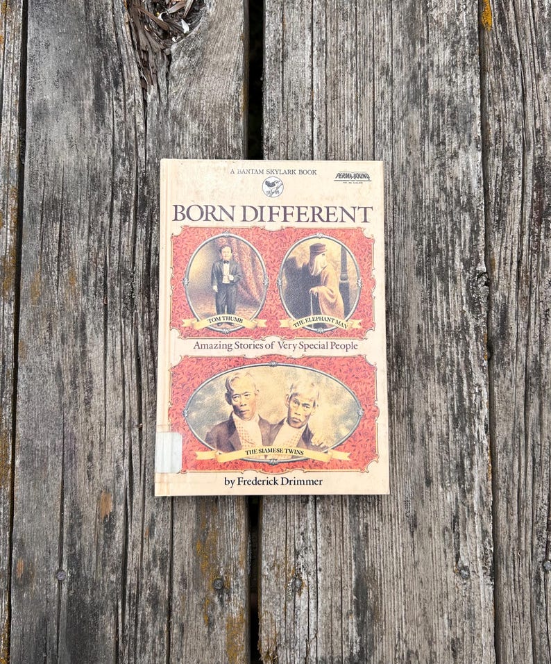 Pu&ograve; includere: Un libro tascabile intitolato Born Different di Frederick Drimmer. La copertina presenta tre ritratti ovali di personaggi storici etichettati come Tom Thumb, The Elephant Man e The Siamese Twins, su uno sfondo rosso a motivi.