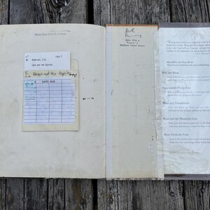 May include: An open vintage library book with a cream-colored interior. The left page features a paper checkout card pocket with a date due slip. The right page contains a printed summary of the Billy and Blaze book series with clear tape.
