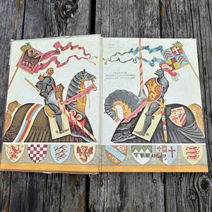 Może przedstawiać: Otwarta stara książka z kolorowymi ilustracjami dw&oacute;ch rycerzy w zbrojach na koniach. Na lewej stronie znajduje się rycerz z czerwoną flagą, a na prawej rycerz z szachownicową flagą oraz tekst Property of Wallowa Public Schools District 66, Wallowa, Ore. i Discarded.