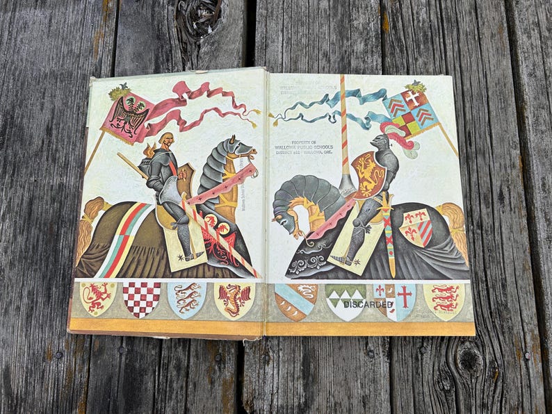 Może przedstawiać: Otwarta stara książka z kolorowymi ilustracjami dw&oacute;ch rycerzy w zbrojach na koniach. Na lewej stronie znajduje się rycerz z czerwoną flagą, a na prawej rycerz z szachownicową flagą oraz tekst Property of Wallowa Public Schools District 66, Wallowa, Ore. i Discarded.