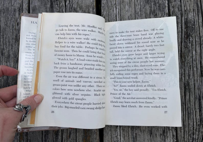 May include: An open book with white pages and black printed text, showing pages 26 and 27. The left page begins with the text Leaving the tent, Mr. Hoeffler said, and the right page ends with the text Zansu liked Ehrich. He even worked with.