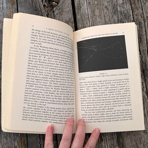 Peut inclure: Un livre ouvert avec du texte et un diagramme sur une surface en bois. Les pages sont jaunies et le texte est en noir. Le diagramme est une illustration en noir et blanc de lignes. Le livre est intitul&eacute; "A Brief History of Time".