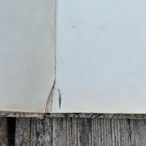 May include: A book with off-white pages showing a visible tear along the central spine gutter. The binding edge features a black and white patterned design, and the paper shows signs of age with slight discoloration and wear along the inner seam.