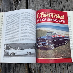 Op de afbeelding: Een open boek met de titel Great Cars From Chevrolet COLOR SHOWCASE II. De pagina toont een donkerblauwe cabriolet geparkeerd bij een strand, met een kleinere zwart-witfoto van een witte cabriolet op de linkerpagina.