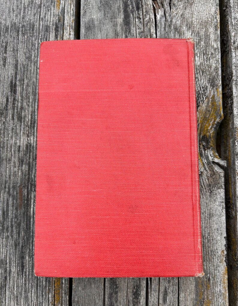 May include: A rectangular hardcover book with a solid, vibrant red fabric cover. The book features a clean, plain front surface with a visible vertical spine edge on the right side, showcasing a simple, uniform texture across the entire front cover.