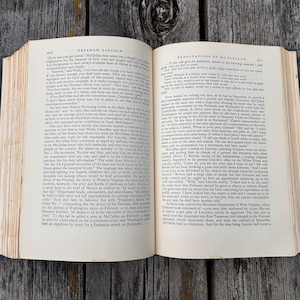 May include: An open hardcover book with cream-colored pages featuring black printed text. The left page is headed Abraham Lincoln and the right page is headed Expectations of McClellan. The book has visible binding and aged paper edges.