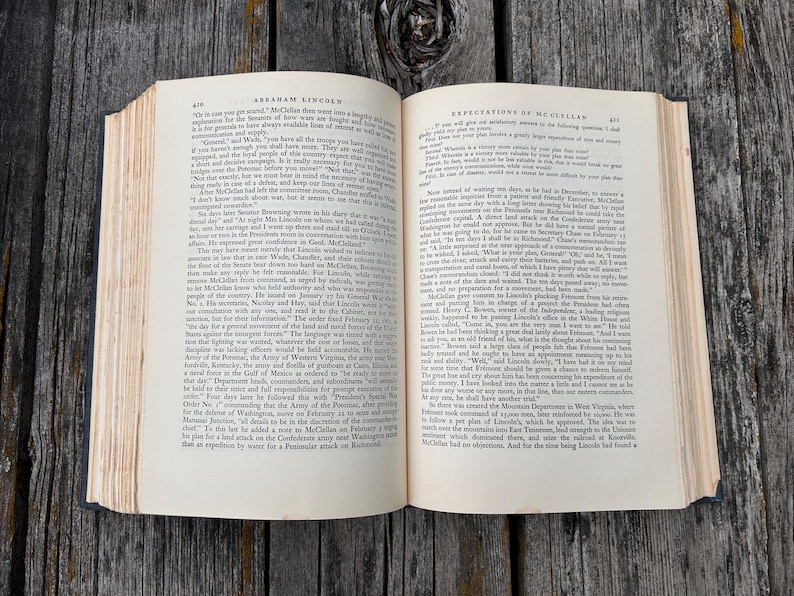 May include: An open hardcover book with cream-colored pages featuring black printed text. The left page is headed Abraham Lincoln and the right page is headed Expectations of McClellan. The book has visible binding and aged paper edges.