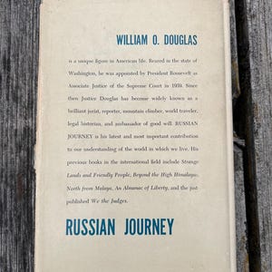 May include: A rectangular book jacket with a cream-coloured background and blue text. The top reads WILLIAM O. DOUGLAS, followed by a biographical paragraph about the author. The bottom features the title RUSSIAN JOURNEY in bold blue lettering.