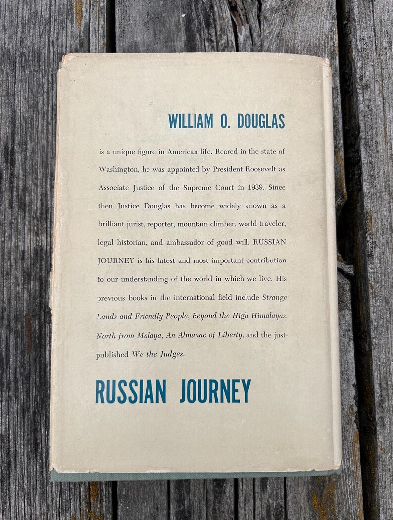 May include: A rectangular book jacket with a cream-coloured background and blue text. The top reads WILLIAM O. DOUGLAS, followed by a biographical paragraph about the author. The bottom features the title RUSSIAN JOURNEY in bold blue lettering.