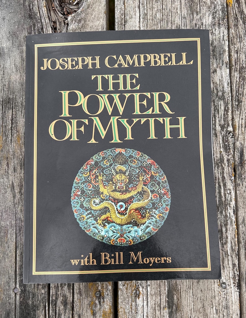 K&ouml;nnte beinhalten: Ein schwarzes Buch mit dem Titel The Power of Myth von Joseph Campbell mit Bill Moyers. Das Cover zeigt goldenen Text und eine kreisf&ouml;rmige, farbenfrohe Illustration eines Drachen, umgeben von komplexen Mustern in Rot, Blau und Gelb.