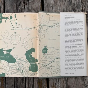 May include: An open book with a cream-coloured map of the U.S.S.R. featuring dark green bodies of water and dashed travel lines. The right page contains a white dust jacket flap with black printed text titled Some conclusions by Justice Douglas.