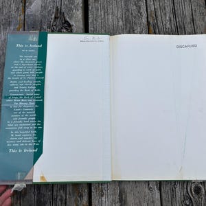 Peut inclure: Un livre reli&eacute; ouvert intitul&eacute; This is Ireland par M. Sasek. Le rabat int&eacute;rieur gauche pr&eacute;sente un texte descriptif sur l'Irlande, tandis que la page de droite est vierge avec le mot DISCARDED imprim&eacute; en noir dans le coin sup&eacute;rieur droit.