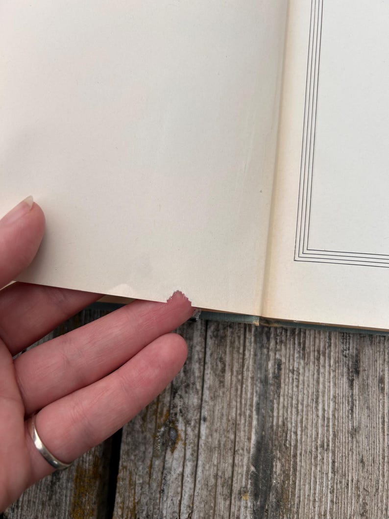 Pu&ograve; includere: Un libro aperto con pagine color bianco sporco che presenta un sottile bordo rettangolare nero sulla pagina destra. Il bordo inferiore della pagina sinistra mostra un piccolo strappo distinto nella carta, con una leggera decolorazione.