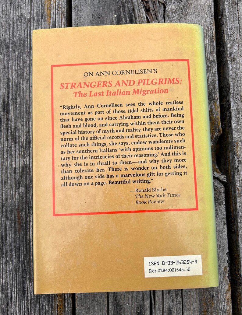 May include: The back cover of a book titled Strangers and Pilgrims: The Last Italian Migration by Ann Cornelisen. It features a tan background with a red-bordered text box containing a review by Ronald Blythe and an ISBN 0-03-063254-4 label.