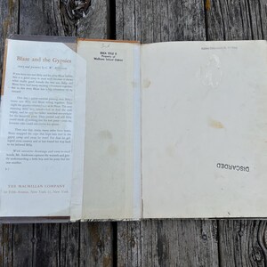 May include: An open hardcover book titled Blaze and the Gypsies by C.W. Anderson, featuring a dust jacket with printed text on the left flap, a cream-colored endpaper with a stamp reading DISCARDED, and a school district property stamp.