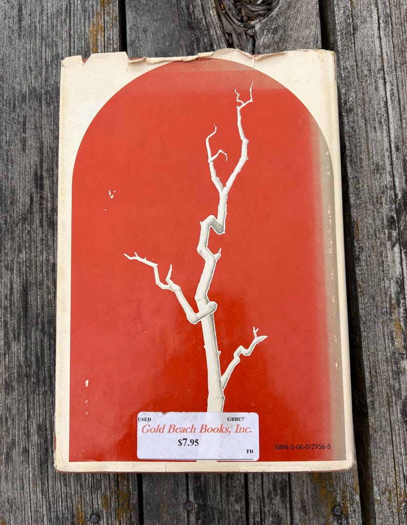 May include: A rectangular book cover featuring a vibrant orange background with a large, white, arched graphic containing a stylized white tree branch. A white rectangular sticker displays the text Gold Beach Books, Inc. and ISBN: 0-06-012956-5.