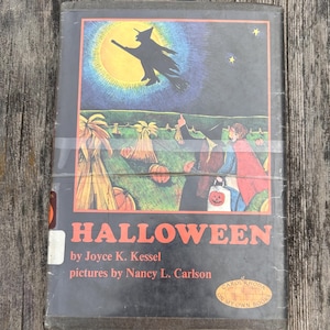 Może przedstawiać: Książka w twardej oprawie zatytułowana Halloween autorstwa Joyce K. Kessel z ilustracjami Nancy L. Carlson. Okładka przedstawia czarną sylwetkę czarownicy lecącej na miotle na tle dużego ż&oacute;łtego księżyca, nad polem z dyniami i dwiema postaciami.